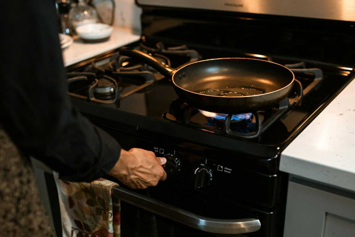 Un uomo che alza il gas sotto una padella in cucina