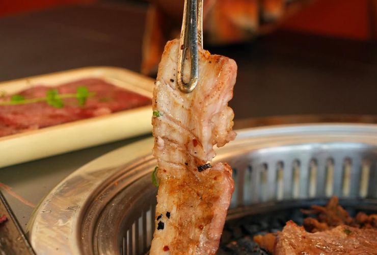 Persona che mette con le pinze il bacon sopra alla griglia posta sul tavolo di un ristorante